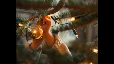 a person holding a christmas ornament up to a tree