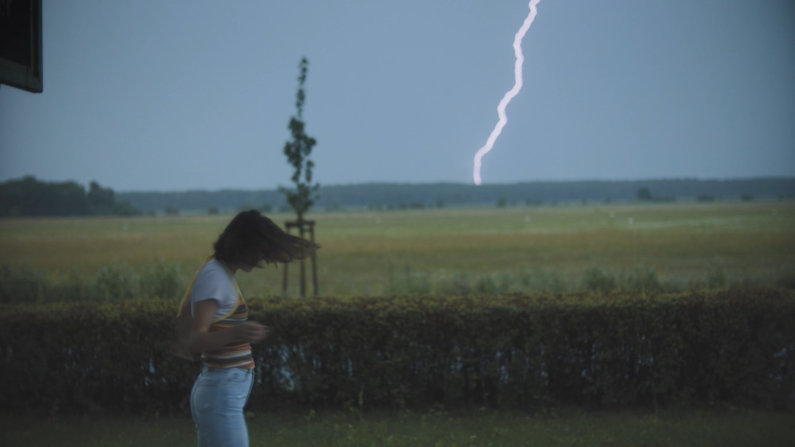 a woman standing in a field with a lightning bolt in the background