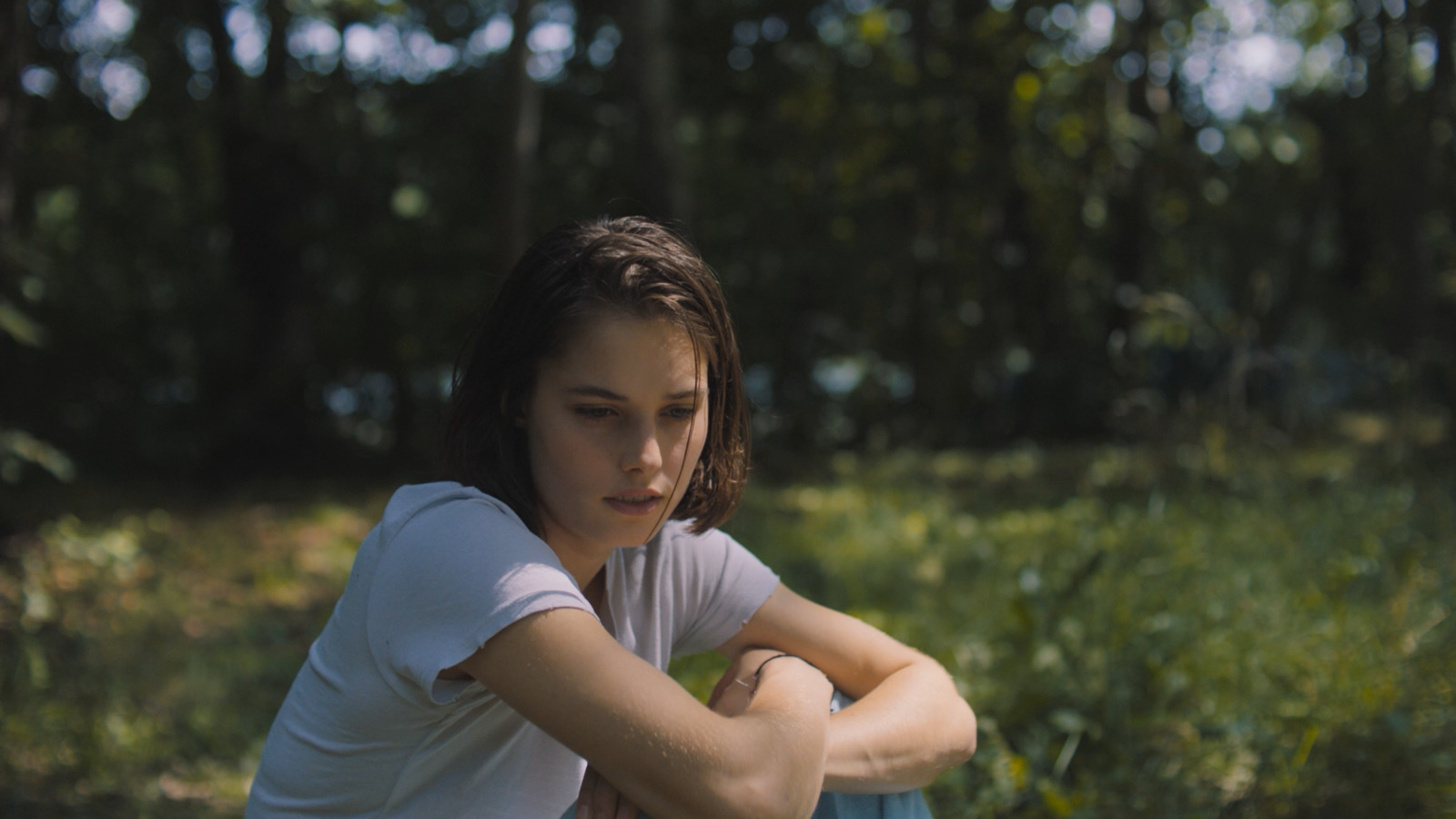 a girl sitting in the grass with her arms crossed