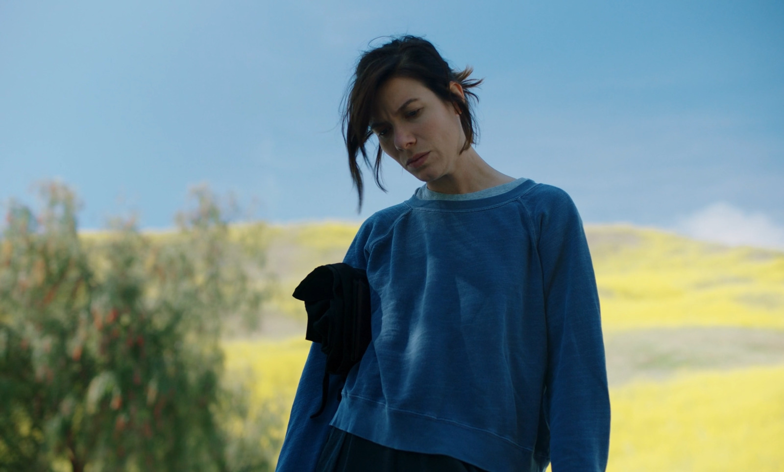a woman standing in a field with a tree in the background