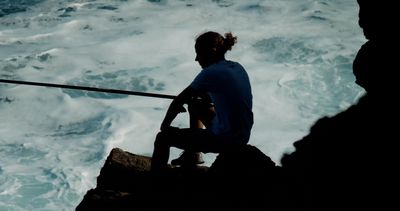 a man sitting on top of a rock next to the ocean