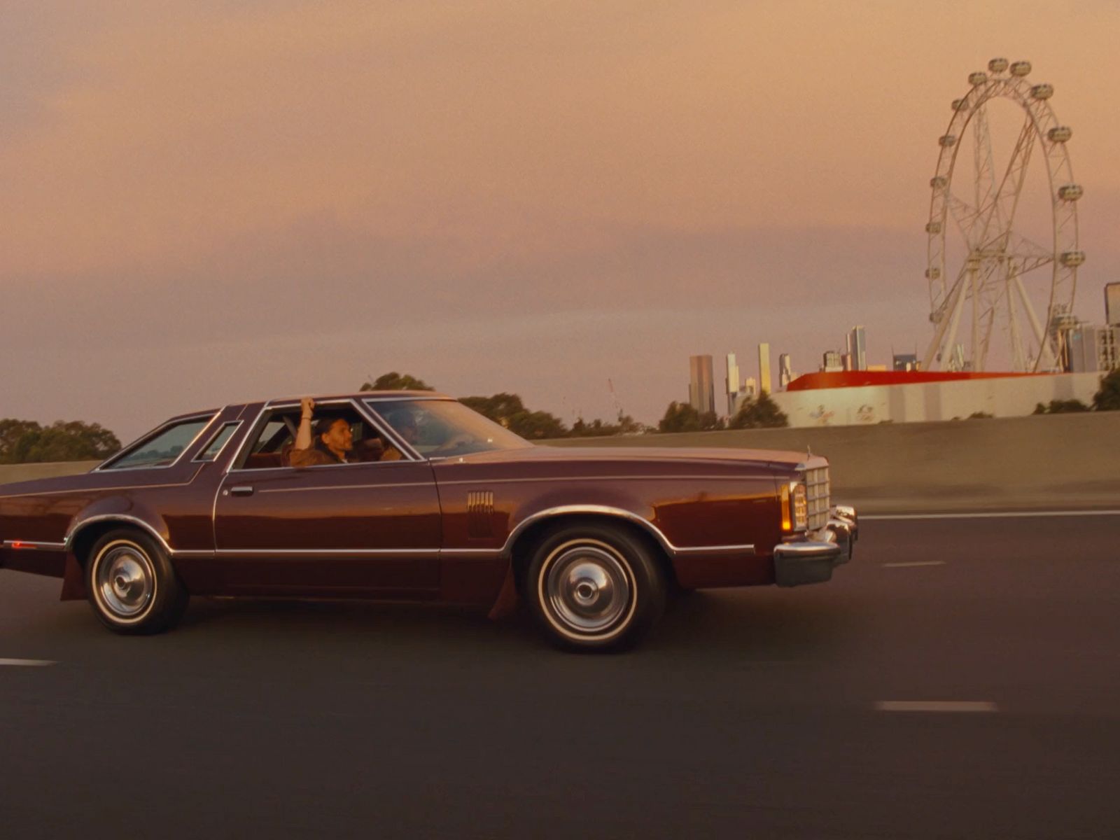 a brown car driving down a street next to a ferris wheel