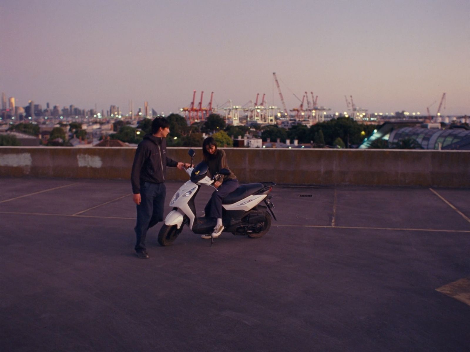 two people standing next to a scooter in a parking lot