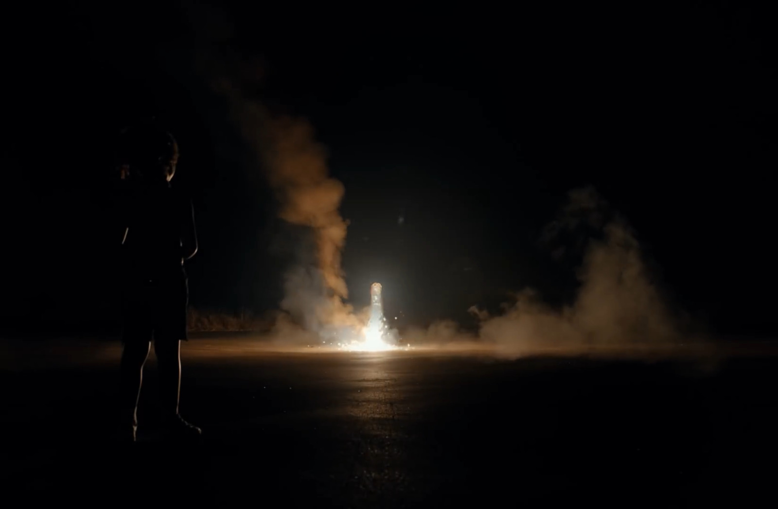 a person standing in the dark with a rocket in the background