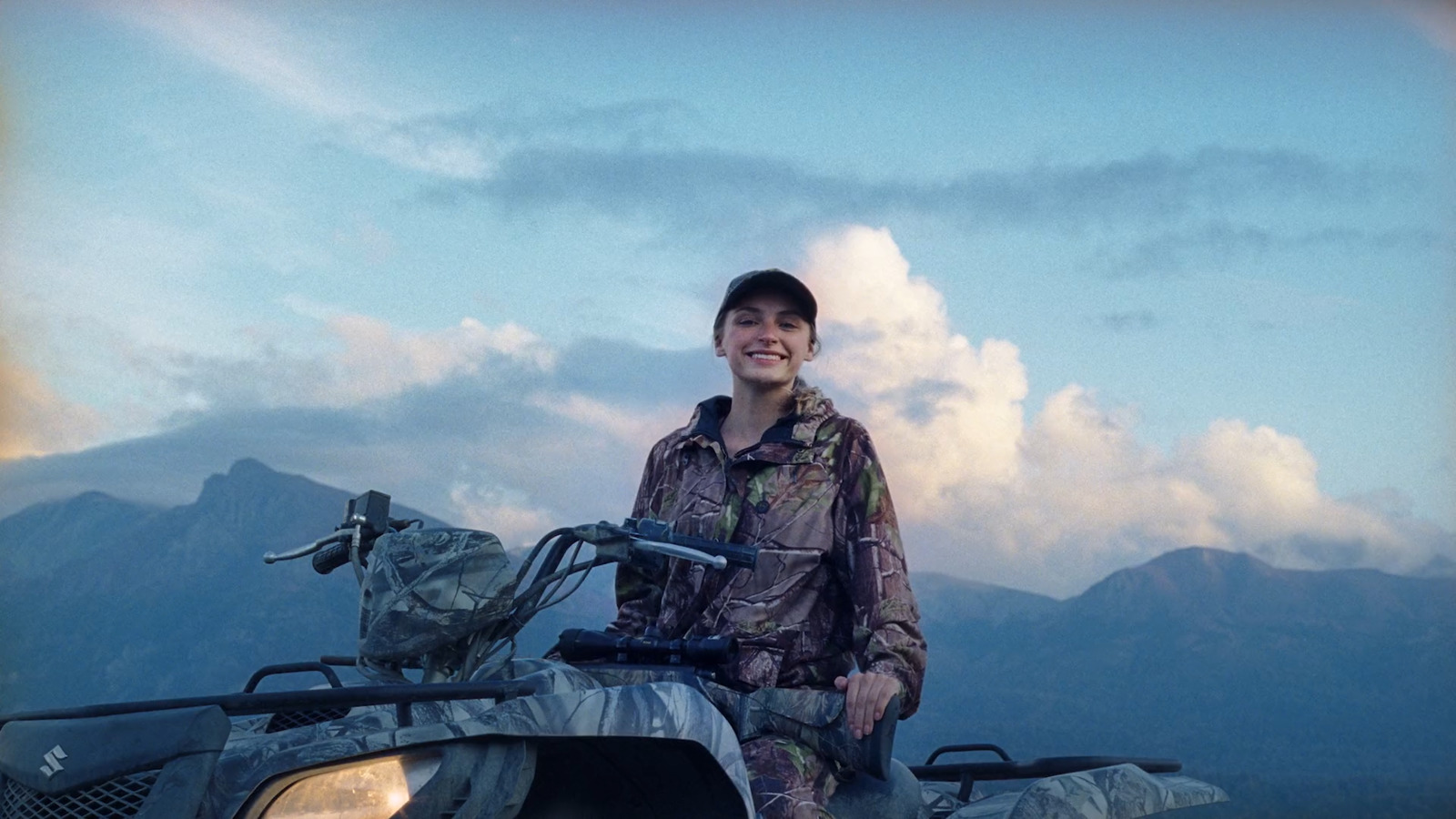 a woman standing next to an atv with mountains in the background