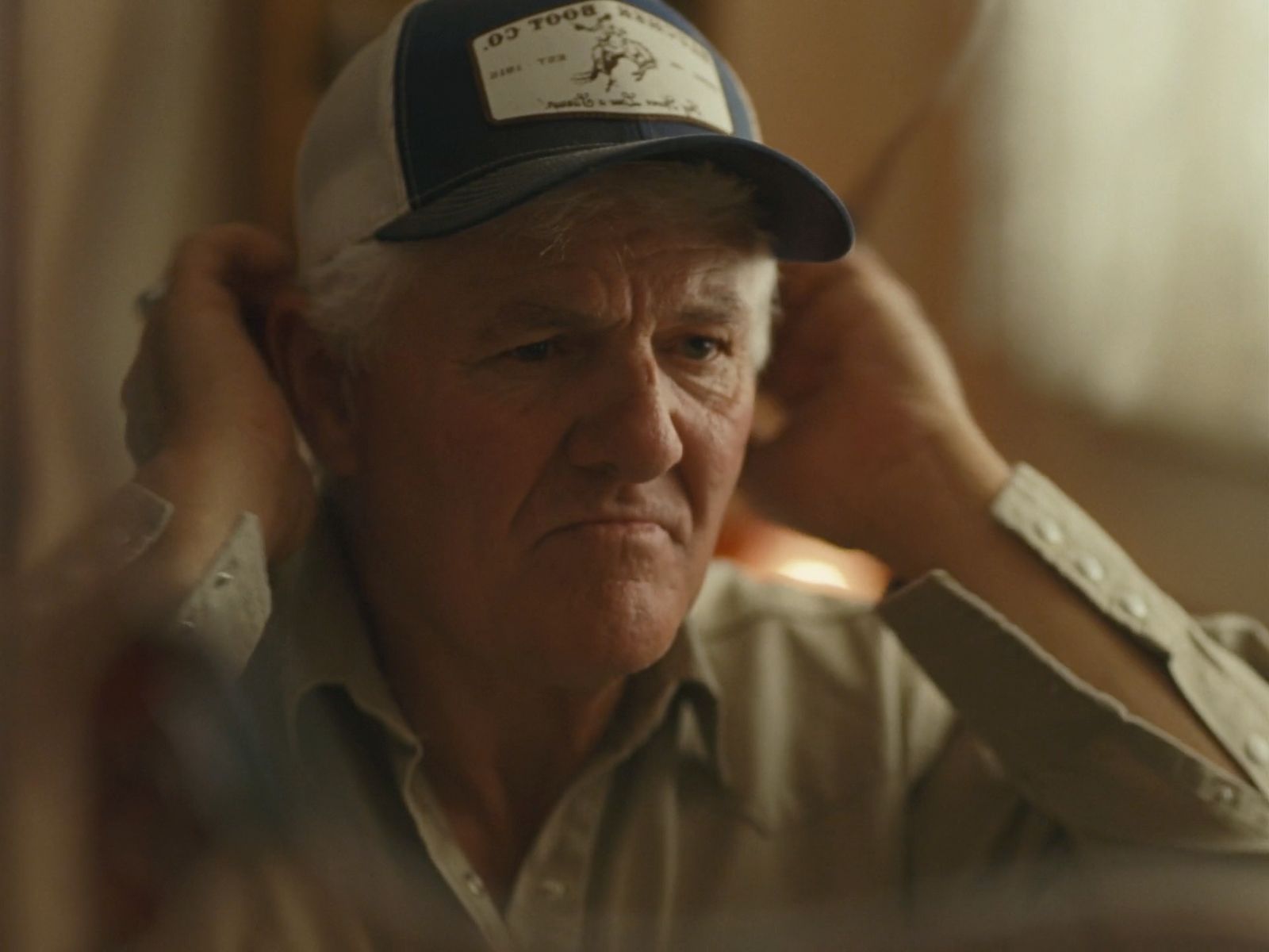 an older man adjusts his hat in a mirror