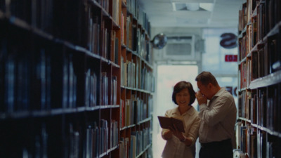 a man and woman standing in a library looking at a book