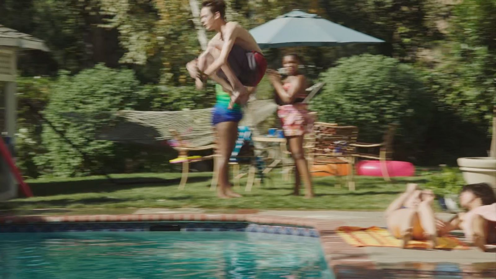 a man jumping into a swimming pool while a woman watches