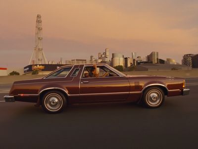 a brown car driving down a street next to a tall building