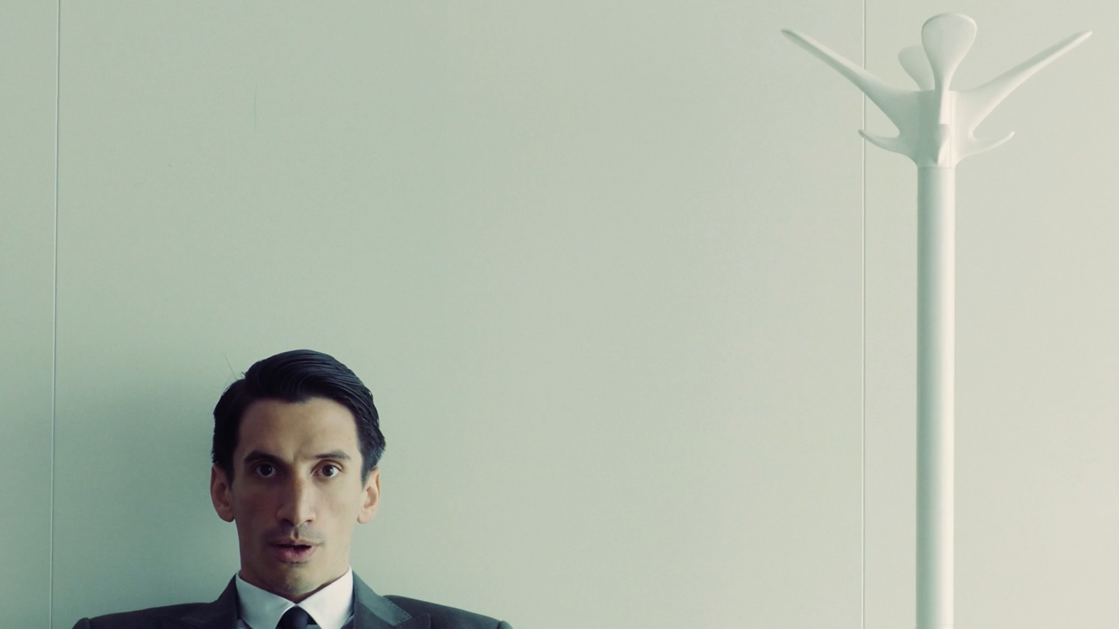 a man in a suit and tie standing in front of a white wall