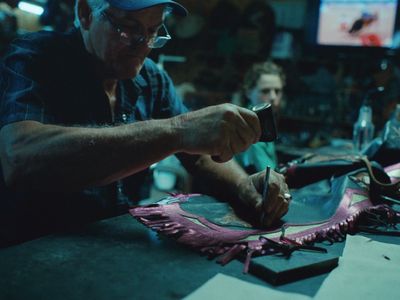 a man cutting a piece of leather with a pair of scissors