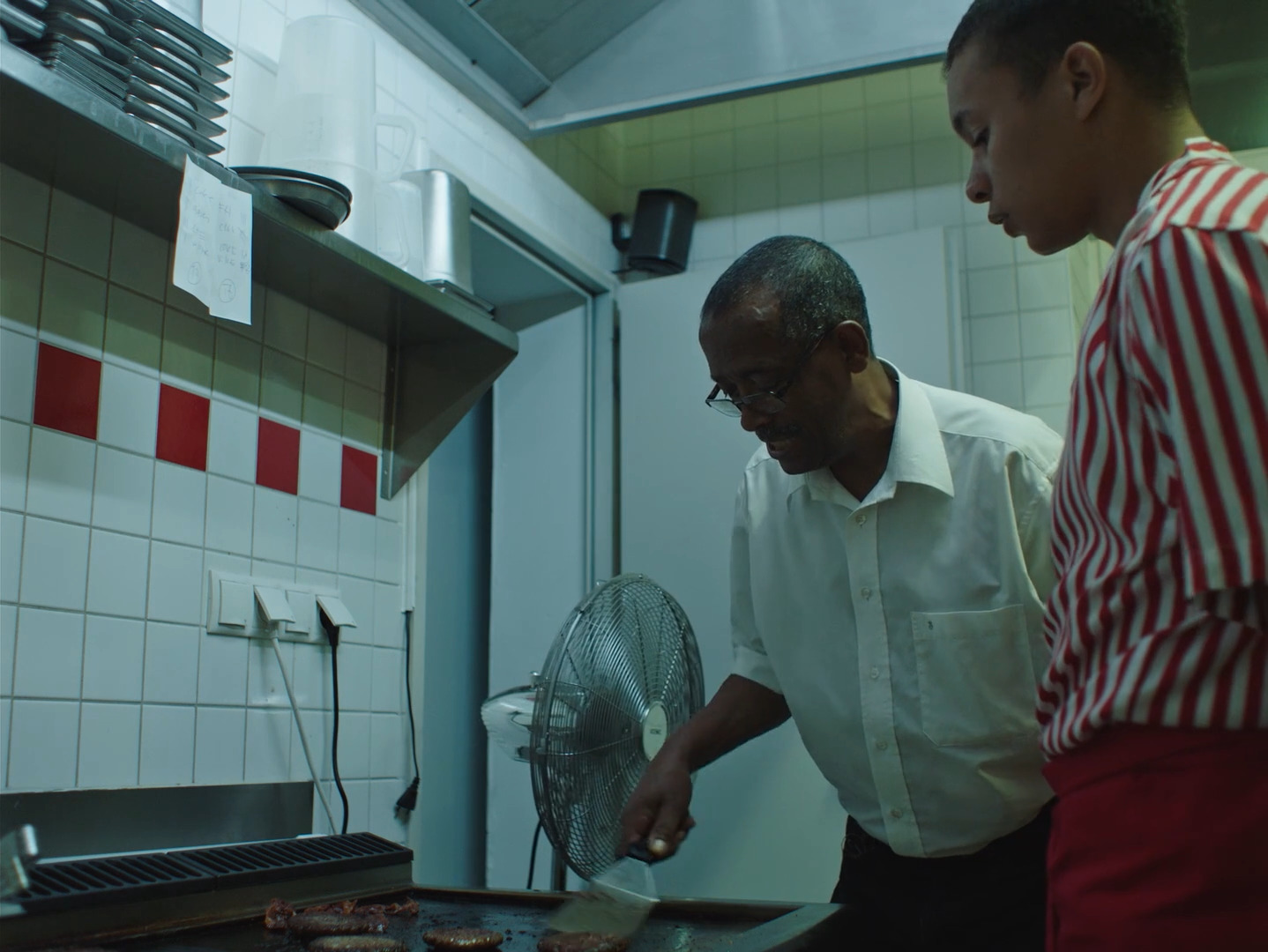 two men in a kitchen preparing food on a grill