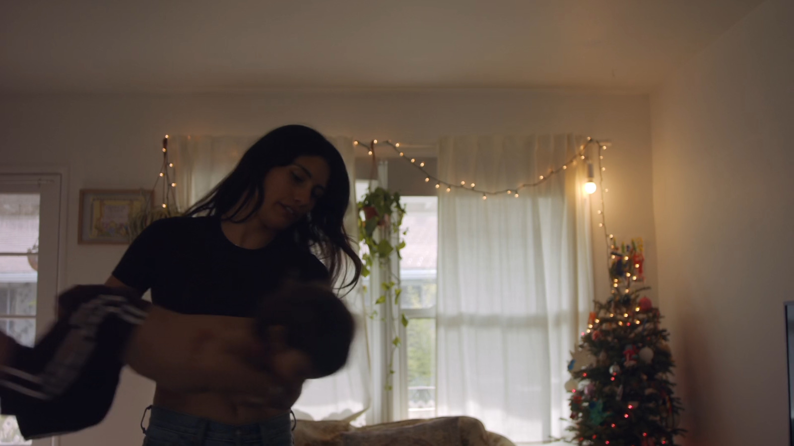 a woman standing in a living room next to a christmas tree