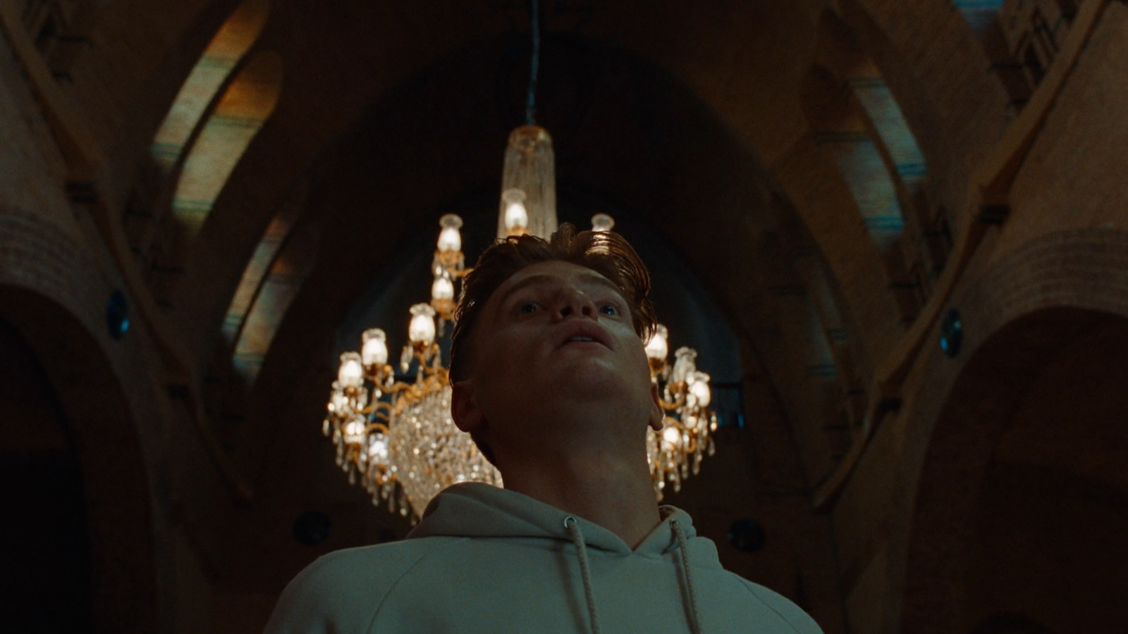 a man in a white hoodie standing in front of a chandelier