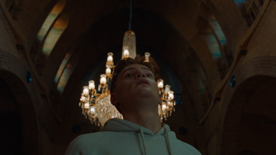 a man in a white hoodie standing in front of a chandelier