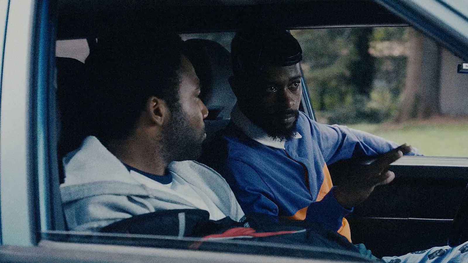 two men sitting in a car looking at a cell phone