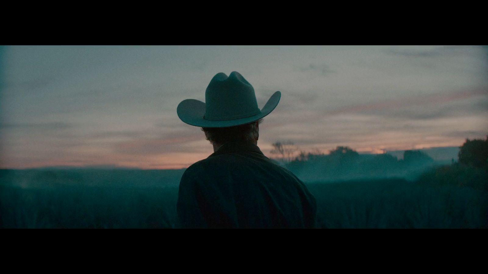 a man wearing a cowboy hat standing in a field