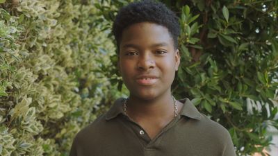 a young man standing in front of a bush