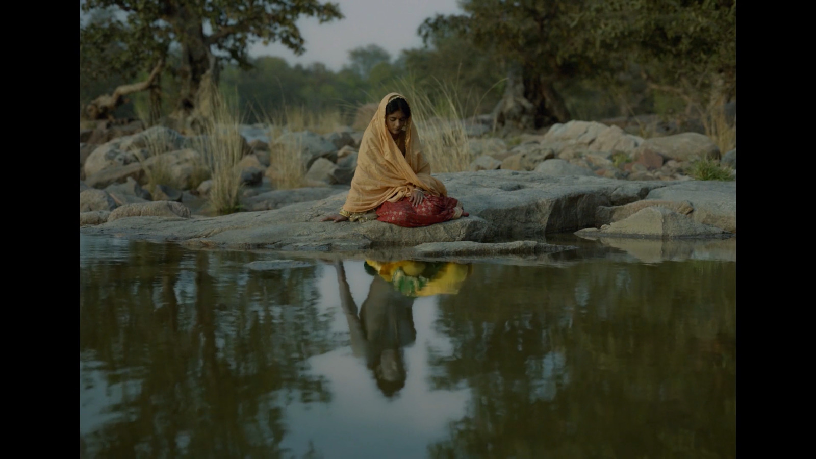 a woman sitting on a rock next to a body of water