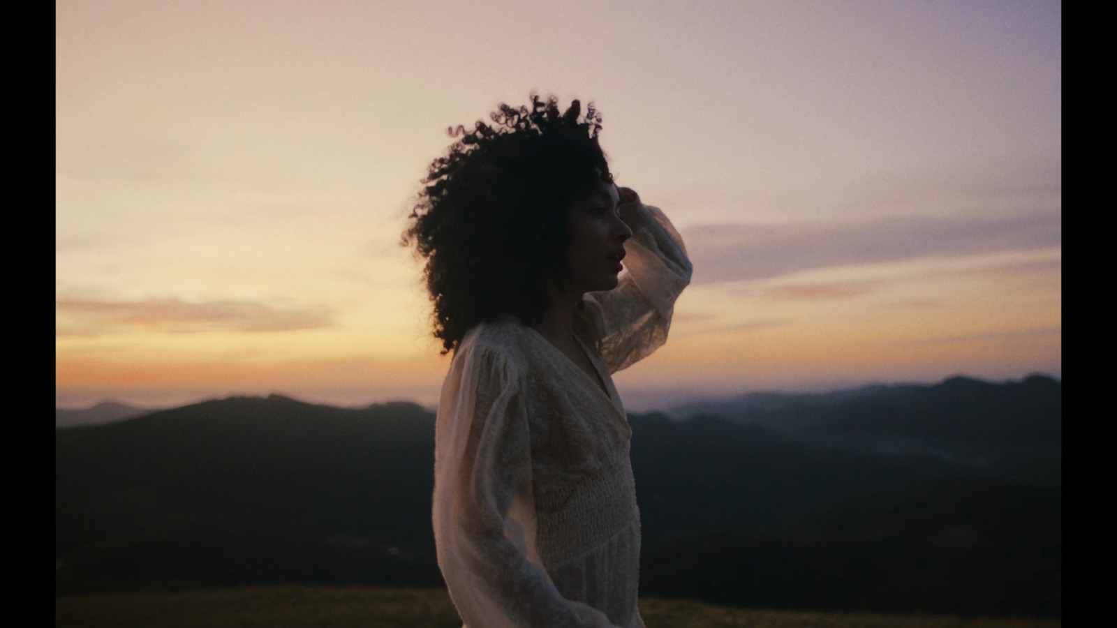 a woman standing on top of a lush green hillside