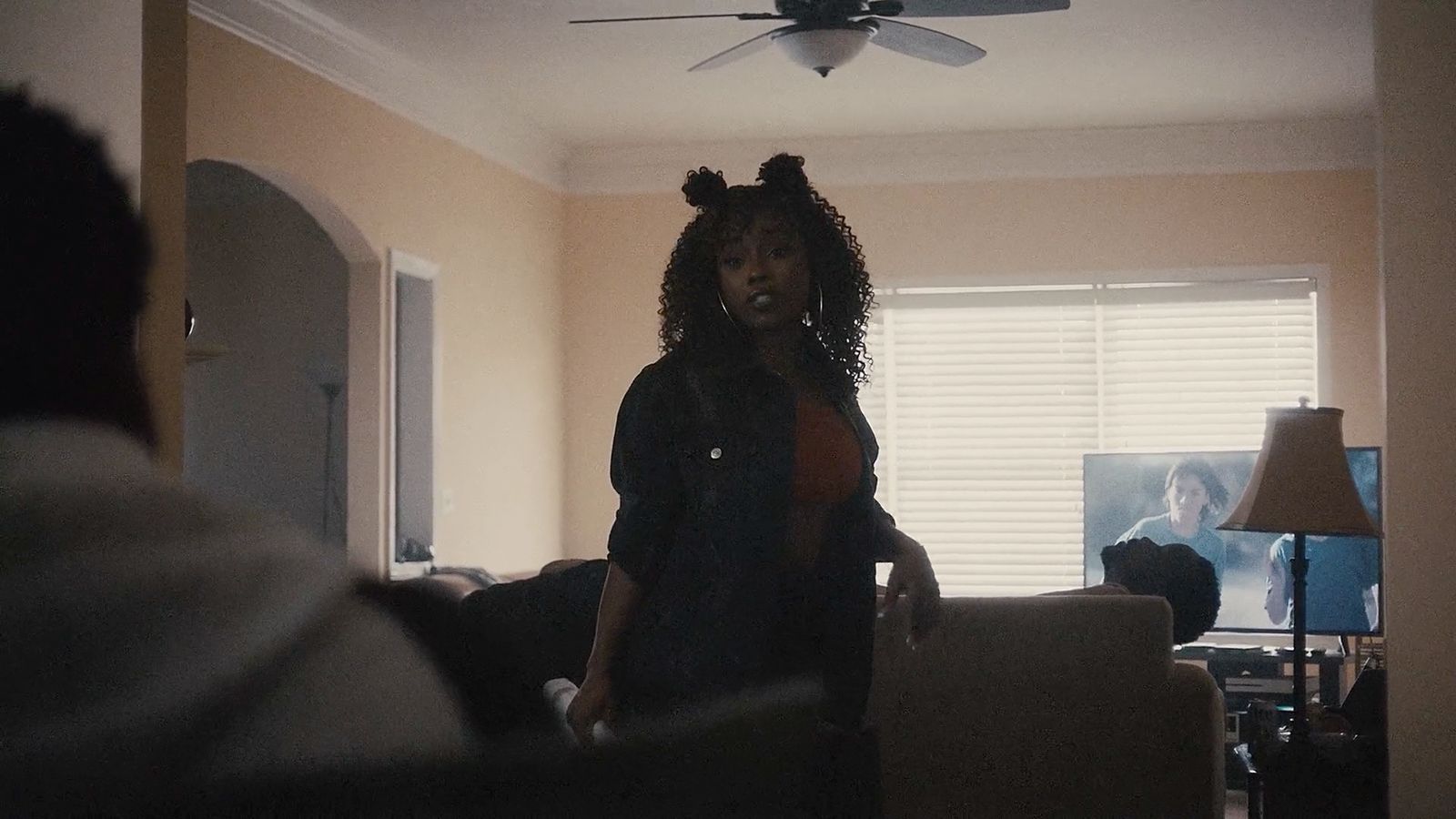 a woman standing in a living room with a ceiling fan