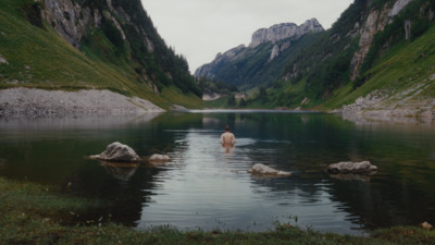 a person wading in a river surrounded by mountains