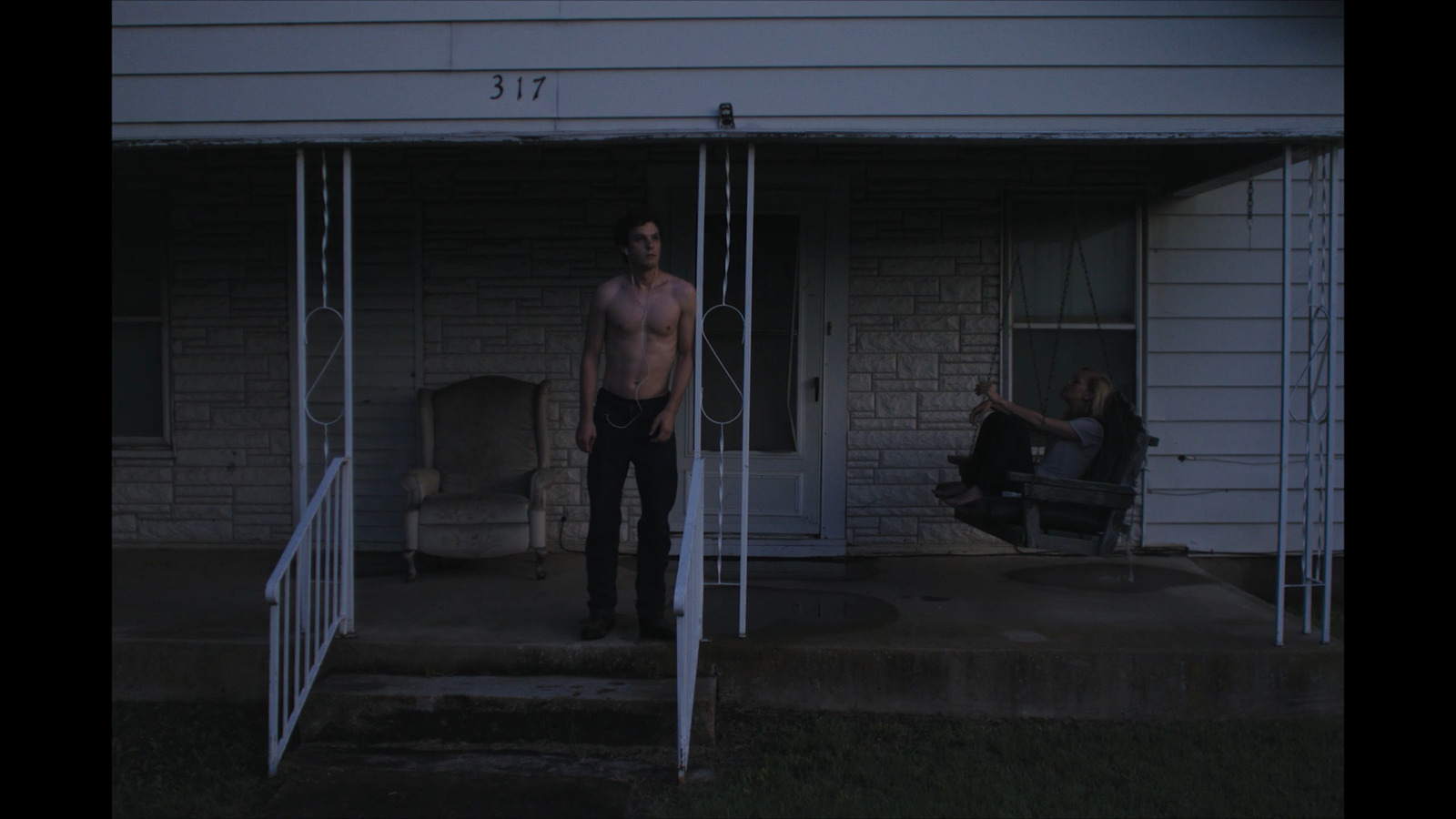 a shirtless man standing in front of a house