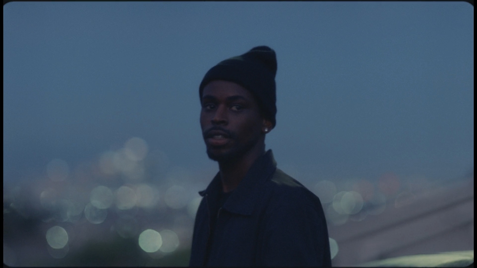 a man with a beanie standing in front of a cityscape