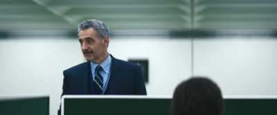 a man in a suit and tie standing in front of a monitor