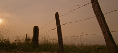 a fence with barbed wire and the sun in the background