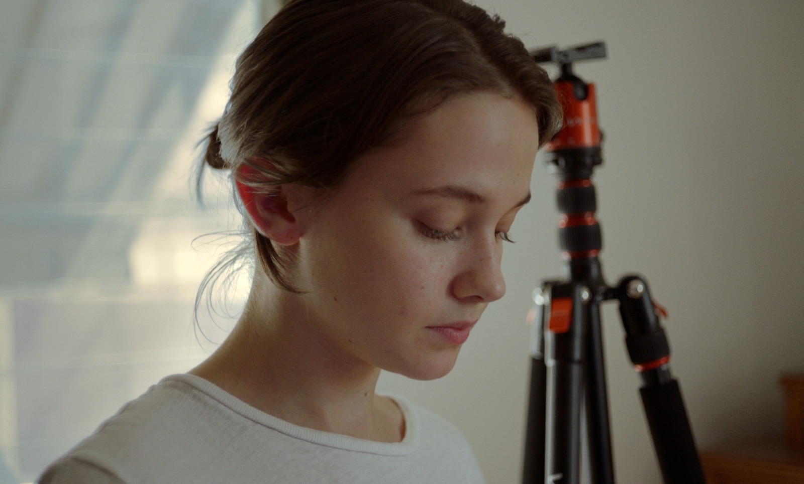 a woman looking down at a camera next to a tripod