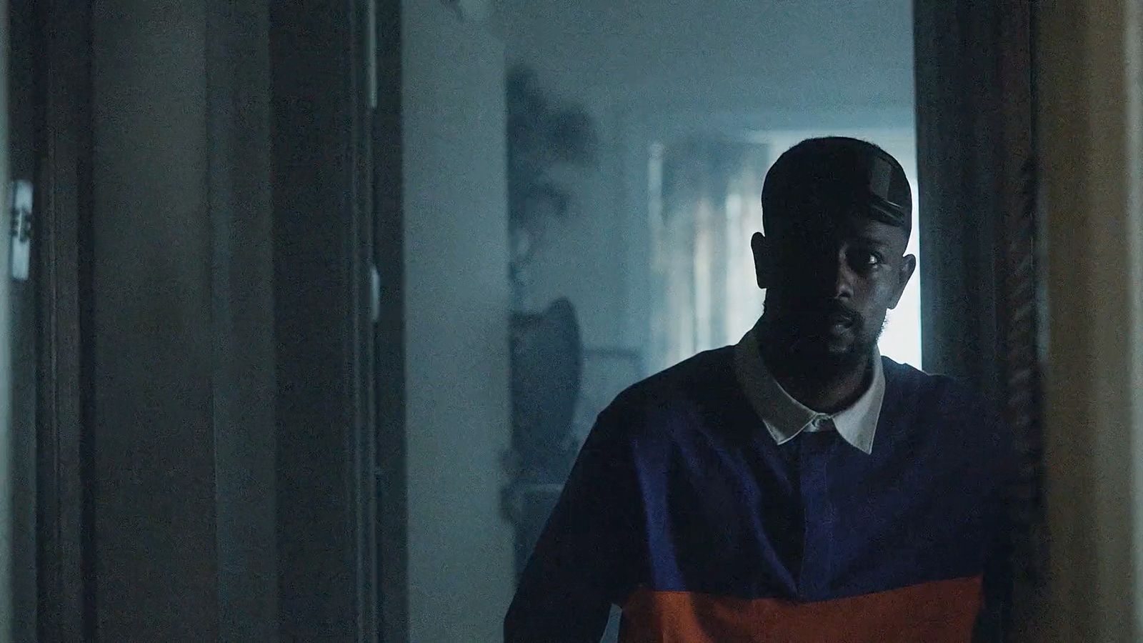 a man in an orange and blue shirt standing in a hallway