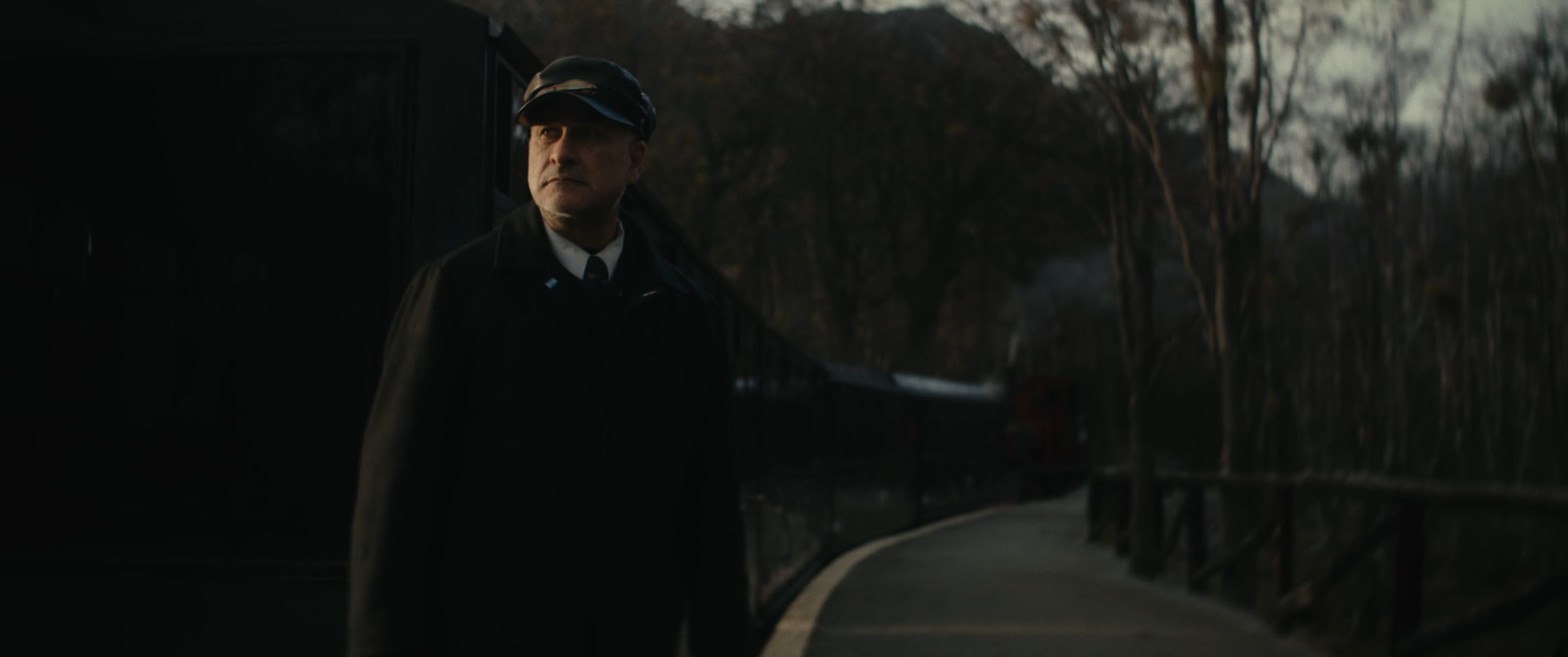 a man in a coat and hat standing next to a train