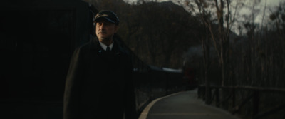 a man in a coat and hat standing next to a train