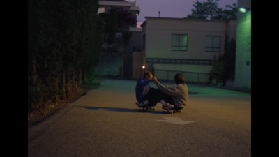 two people sitting on a skateboard in the street