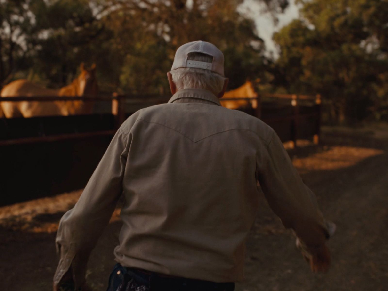 a man walking down a dirt road next to a fence