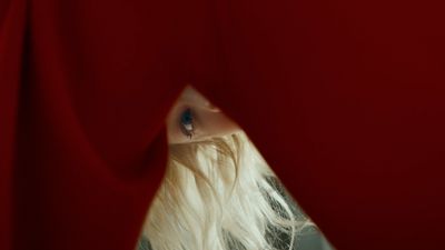 a woman with long white hair looking out of a red curtain