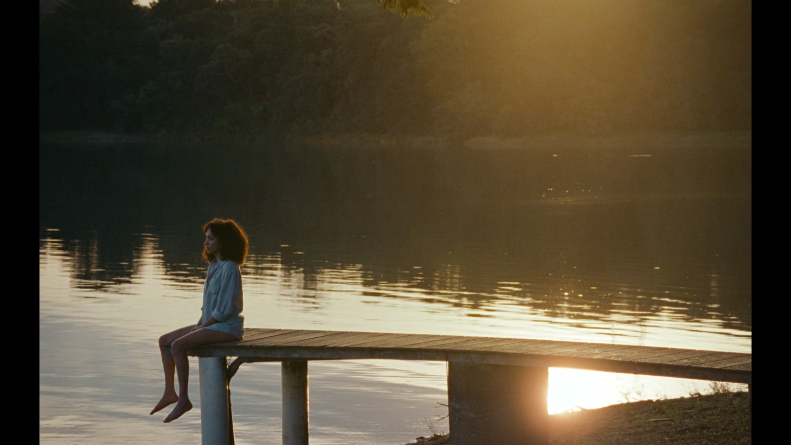 a woman sitting on a dock watching the sun go down