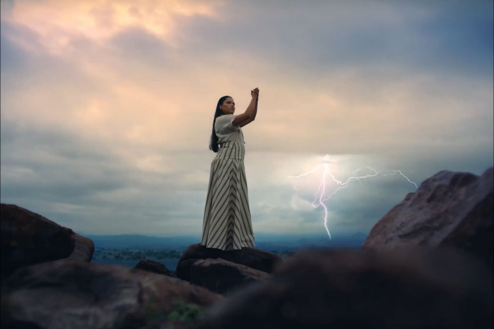 a woman standing on top of a large rock under a cloudy sky