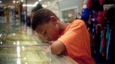 a young boy leaning on a glass shelf in a store