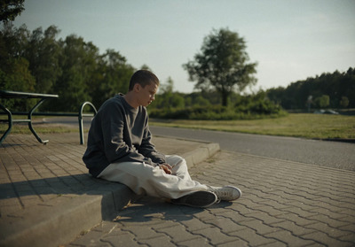 a young man sitting on the ground next to a park bench