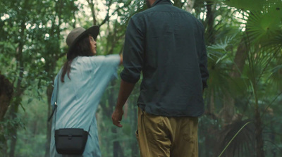 a man and woman walking through a forest holding hands