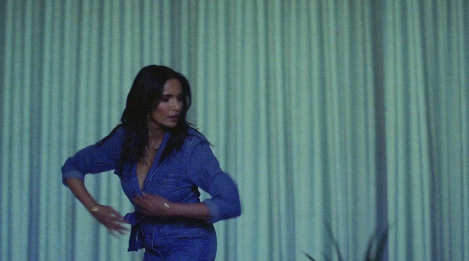 a woman in a blue jumpsuit standing in front of a curtain