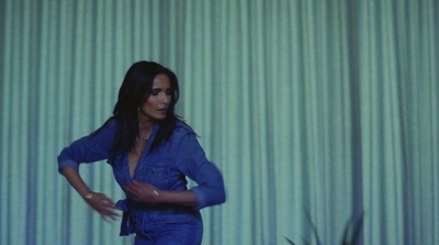 a woman in a blue jumpsuit standing in front of a curtain