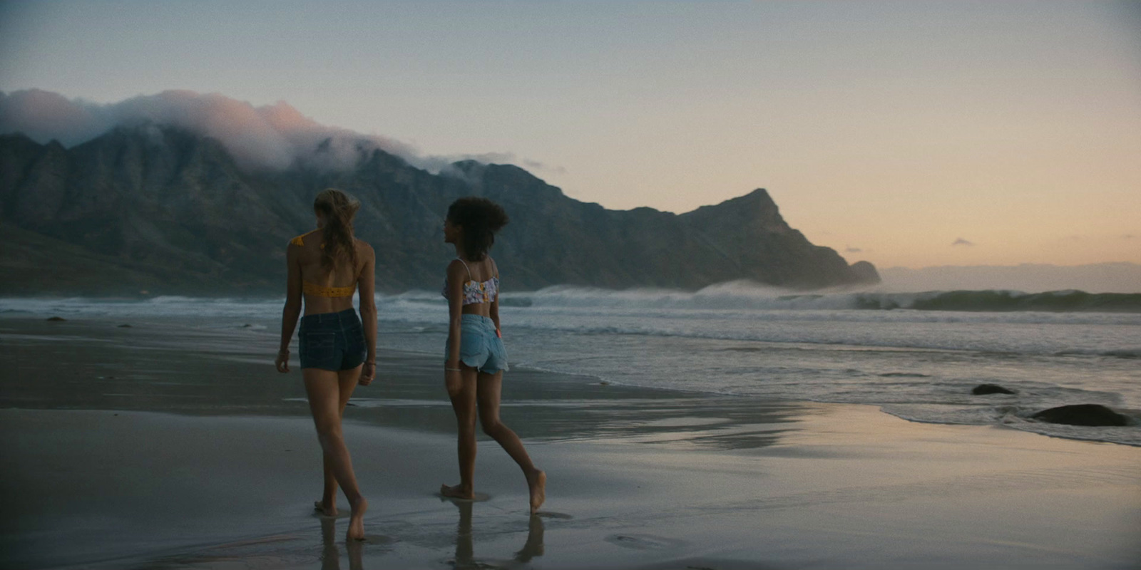 two girls standing on a beach with mountains in the background