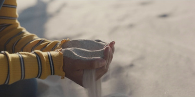 a person's hands are in the sand holding a piece of sand