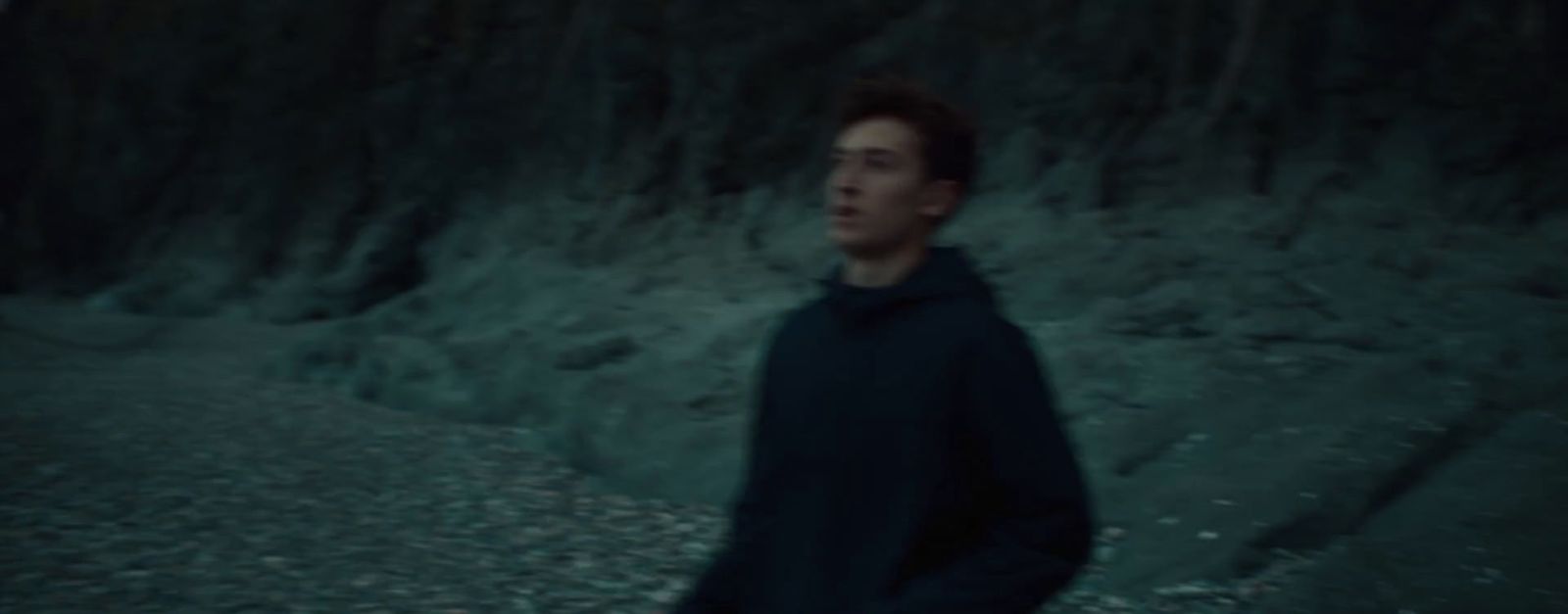 a man in a black hoodie standing in front of a mountain