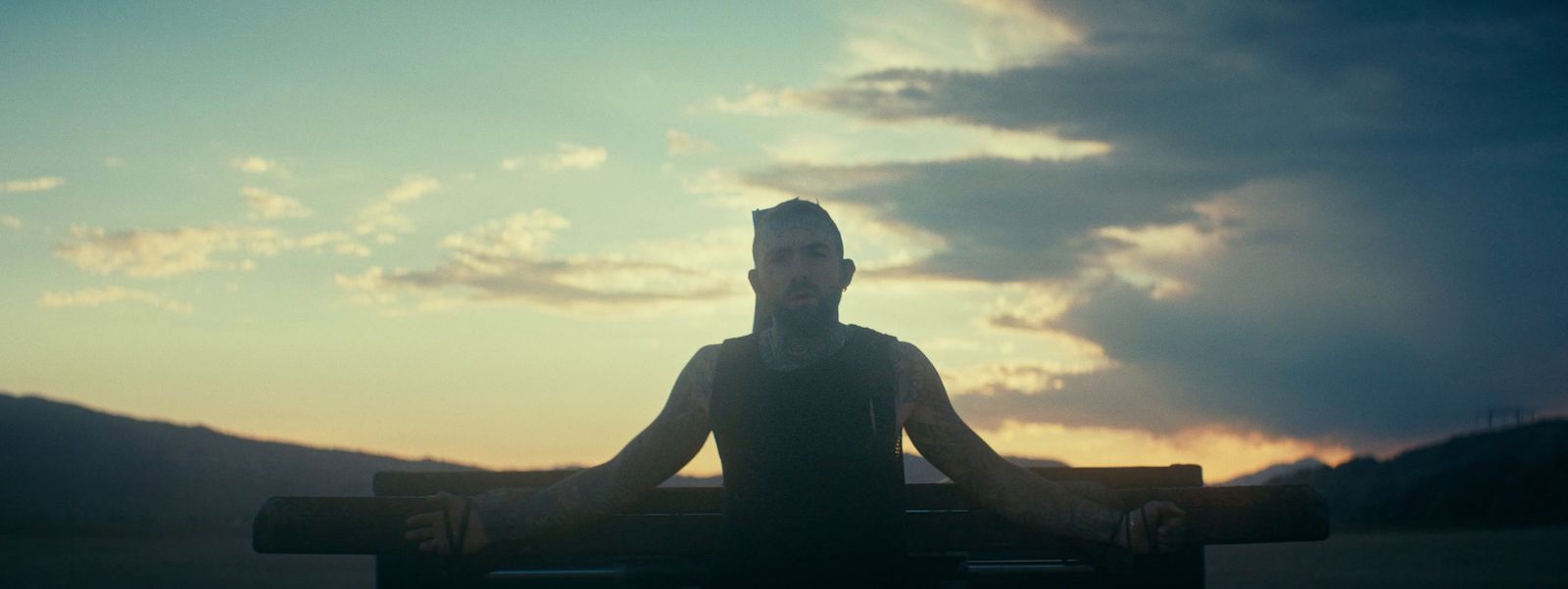 a man sitting on a bench in front of a sunset