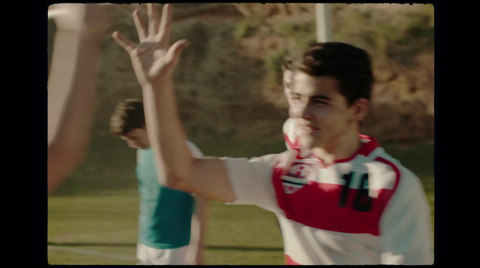 a young man is waving to another man on the soccer field