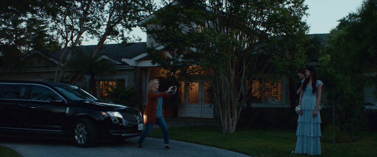 a woman standing next to a black car in front of a house